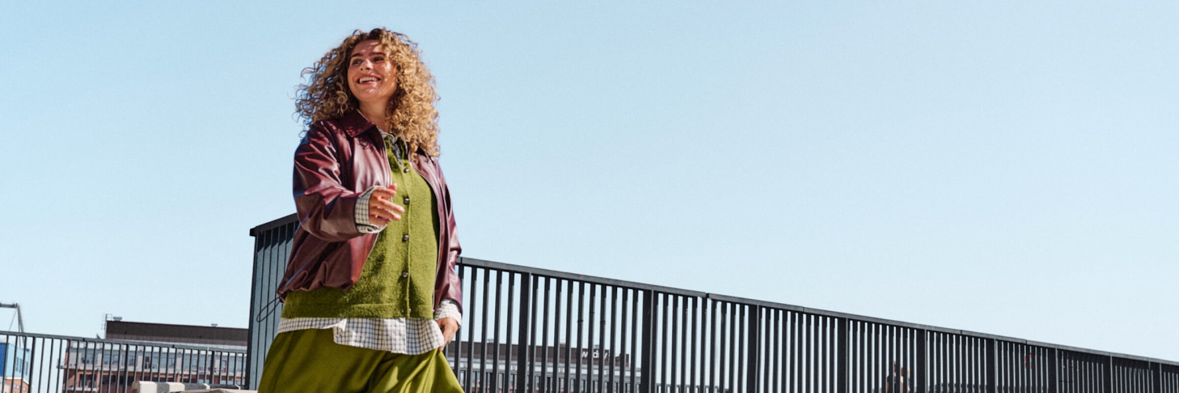 Model in een vloeiende groene satijnen rok, groene trui en bordeauxrode jas die een trap afloopt